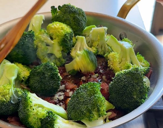 Frying broccoli, bacon and garlic in a pan.