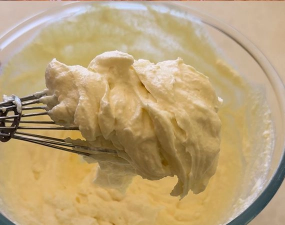 A whisk loaded up with whipped ricotta and cream cheese.