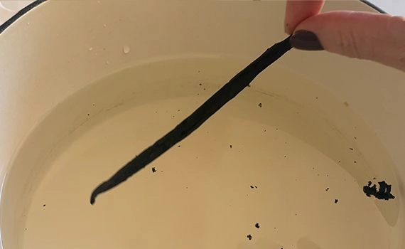 Adding a vanilla bean to a pot of water with sugar