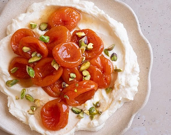 A plate of whipped ricotta, roached apricots and pistachios.