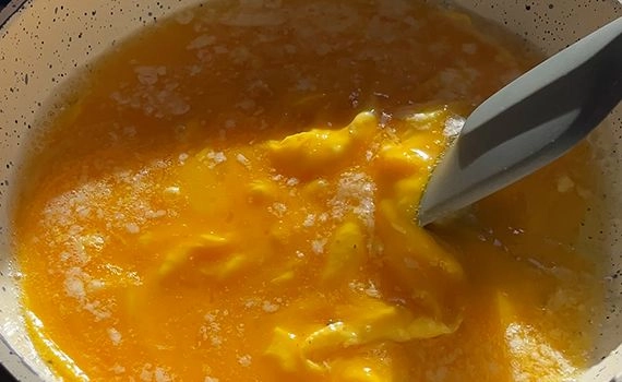 Eggs starting to cook, a spatula moving the cooked egg to the centre of the pan