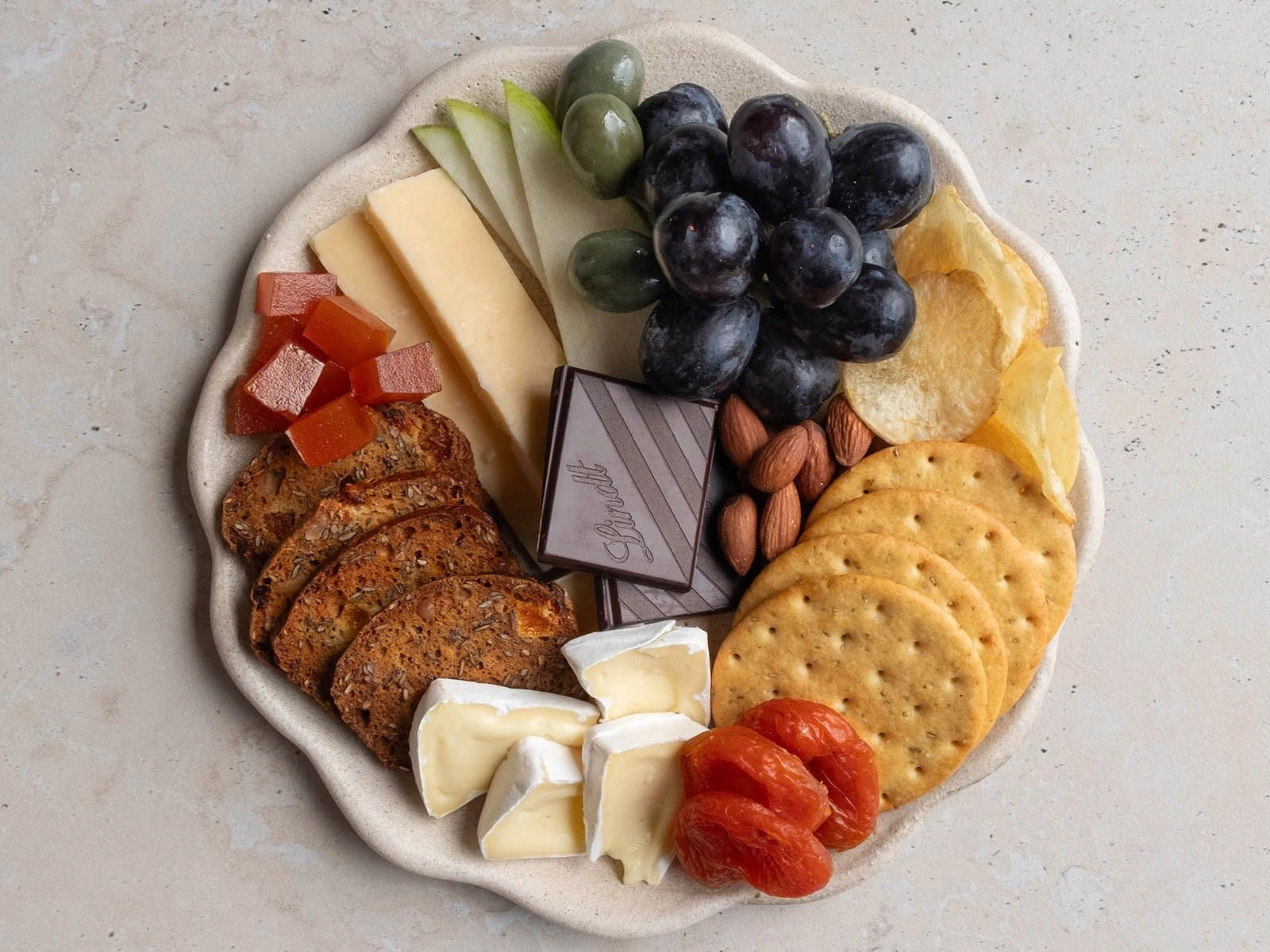 A charcuterie board lunch plate with crackers, cheese, fruit, nuts and chocolate.