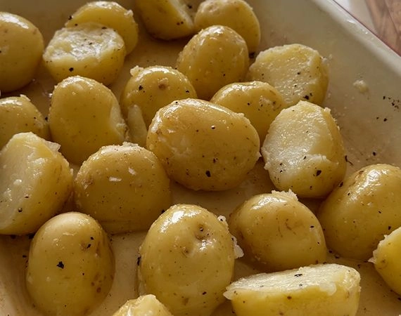 Beef tallow, salt and pepper added to potatoes in a roasting tray