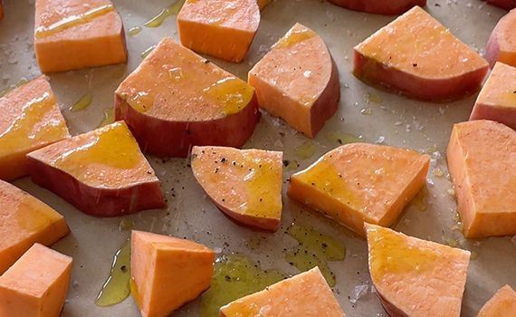 Sweet potatoa chopped on a baking tray with salt, pepper and olive oil 
