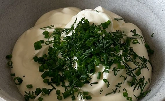 Chopped dill and chives added to a bowl of creme fraiche