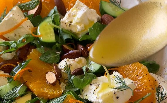 Adding dressing to the orange feta and almond salad