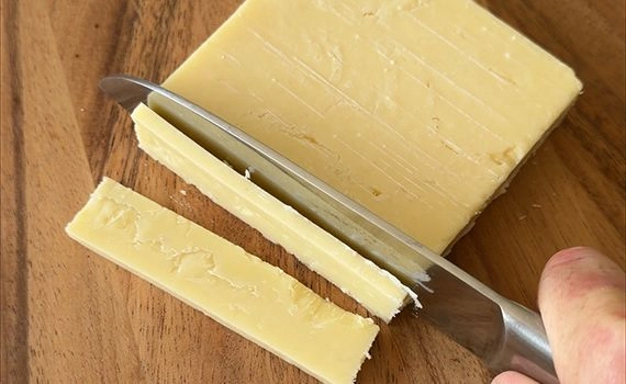 A cheddar block being sliced