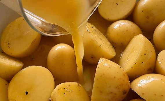 Chicken stock being added to cut potatoes in a roasting tray