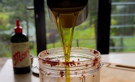 Olive oil being added to a container with sun-dried tomato pesto.