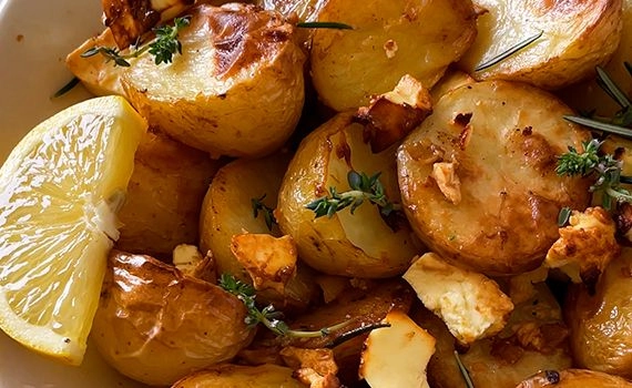 Close up of lemon feta potatoes with fresh thyme and rosemary, and a slice of lemon.