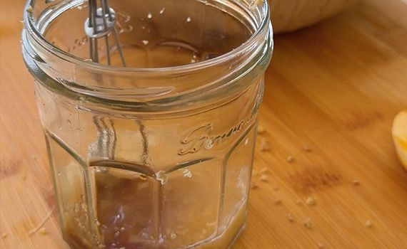 Ingredients to make a salad dressing added to a jar with a whisk