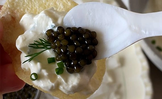 Adding caviar to a potato chip with creme fraiche, dill and chives