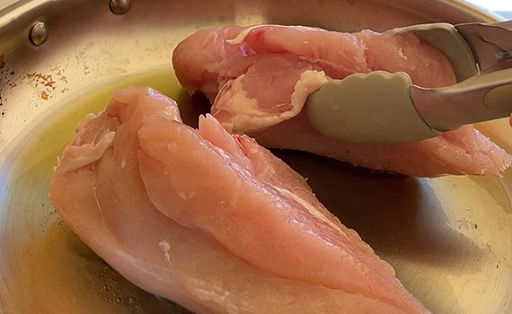 Chicken breast being seared in a pan
