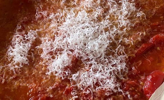 Adding grated parmesan to the roasted tomato sauce