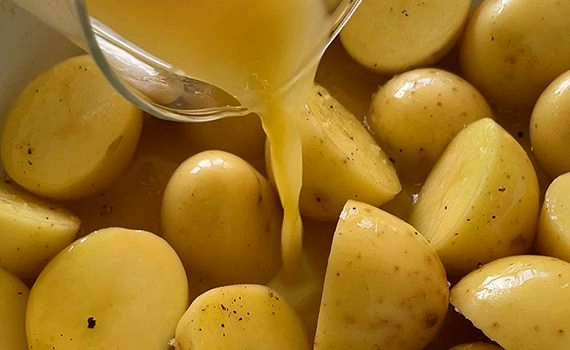 Adding chicken stock to baby potatoes in a tray.